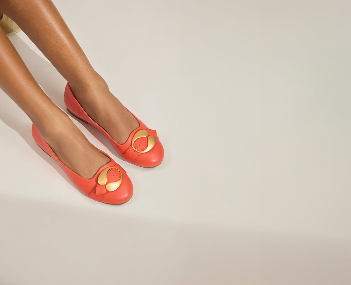 Coral flats with gold heart designs on a light background